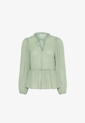 Könnyű zöld blúz hosszú ujjakkal, V-nyakkal, nyaklánc-csokor részlettel és fekete pöttyös mintával; peplum aljjal és ráncolt ujjakra jellemző.