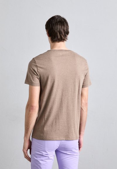T-shirt masculina em castanho, de mangas curtas, com decote redondo, feito de um tecido suave com uma textura lisa, combinado com calças lilás claras.