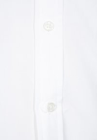 Weißes Hemd mit Knopfleiste, das eine glatte Textur aufweist, mit zwei sichtbaren weißen Knöpfen und einem klaren, einfachen Design ohne Muster.