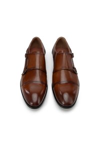 Zapatos de cuero marrón con un acabado suave, punta afilada, dos correas con hebillas y acentos de costura en contraste, situados sobre un fondo blanco.