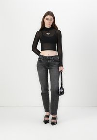 Black sheer long-sleeve crop top with logo, paired with faded gray straight-leg jeans. Model carries a small black handbag and wears pointed heels.