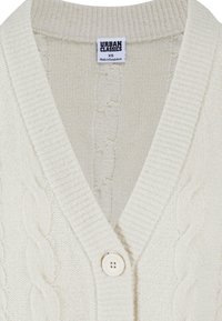 Cremfarbener Strickcardigan mit V-Ausschnitt, Kabelstrickmuster, gerippten Kanten und einem einzigen weißen Knopfverschluss. Etikett: URBAN CLASSICS.