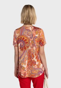 Haut à manches courtes avec un motif cachemire vibrant en orange, rouge et violet sur un fond clair, doté d'un ourlet arrondi et d'une coupe décontractée.