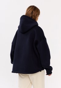 Felpa oversize blu navy realizzata in tessuto morbido. Presenta un grande cappuccio e spalle abbassate, con una vestibilità rilassata e polsini a costine.