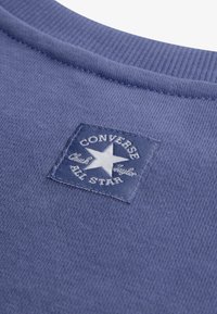 Μπλε βαμβακερό φούτερ με ριμπ στρόγγυλη λαιμόκοψη, που διαθέτει υφασμάτινη ετικέτα με λευκό κείμενο και γραφικό αστέρι, γράφοντας "Converse Chuck Taylor All Star."