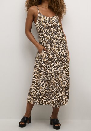 Mujer con vestido midi sin mangas de estampado de leopardo con bolsillos y tacones plataforma abiertos de color negro, de pie frente a un fondo liso.