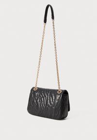Black quilted handbag with gold chain strap and leather shoulder pad, set against white background.