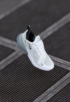 White athletic sneaker with perforated mesh upper, black accents, visible laces, and a translucent air cushioning sole.