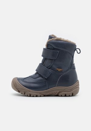 Botte d'hiver bleu marine pour enfants avec deux sangles en velcro, semelle marron robuste et doublure en fourrure beige douce visible en haut.