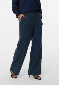 Breda byxor i mörkblått tyg, med en slät yta, sidofickor och skräddarsydd passform, i kombination med svarta högklackade sandaler.