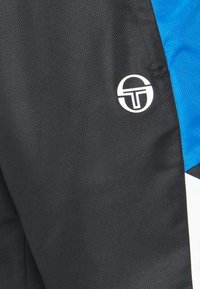 Shorts de sport noirs en tissu texturé, dotés d'un panneau bleu et d'un logo circulaire blanc à l'avant. Design athlétique moderne.