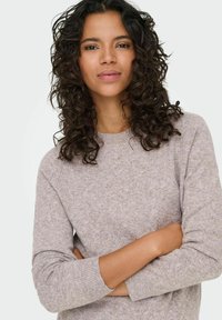 Pull en maille beige clair avec un col rond, motif texturé et manches longues, doté de poignets côtelés et d'une coupe décontractée.
