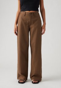 Braune weit geschnittene Hosen mit strukturierter Oberfläche, ausgestattet mit einem vorderen Knopfverschluss, seitlichen Taschen und einem knöchellangen Saum.