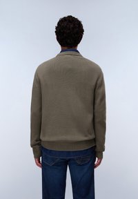 Olivgrüner Strickpullover mit Rundhalsausschnitt und gerippten Bündchen, kombiniert mit blauen Denim-Jeans. Strukturierter Stoff mit lässiger Passform.