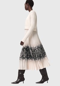 Maglione bianco corto abbinato a un abito maxi plissettato con un motivo grafico bianco e nero all'orlo, completato da stivali alti fino al ginocchio.