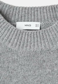Maglione grigio a maglia con un collo a coste. Il tessuto presenta una finitura morbida e testurizzata. Le etichette indicano la taglia M per Europa, USA e Messico.