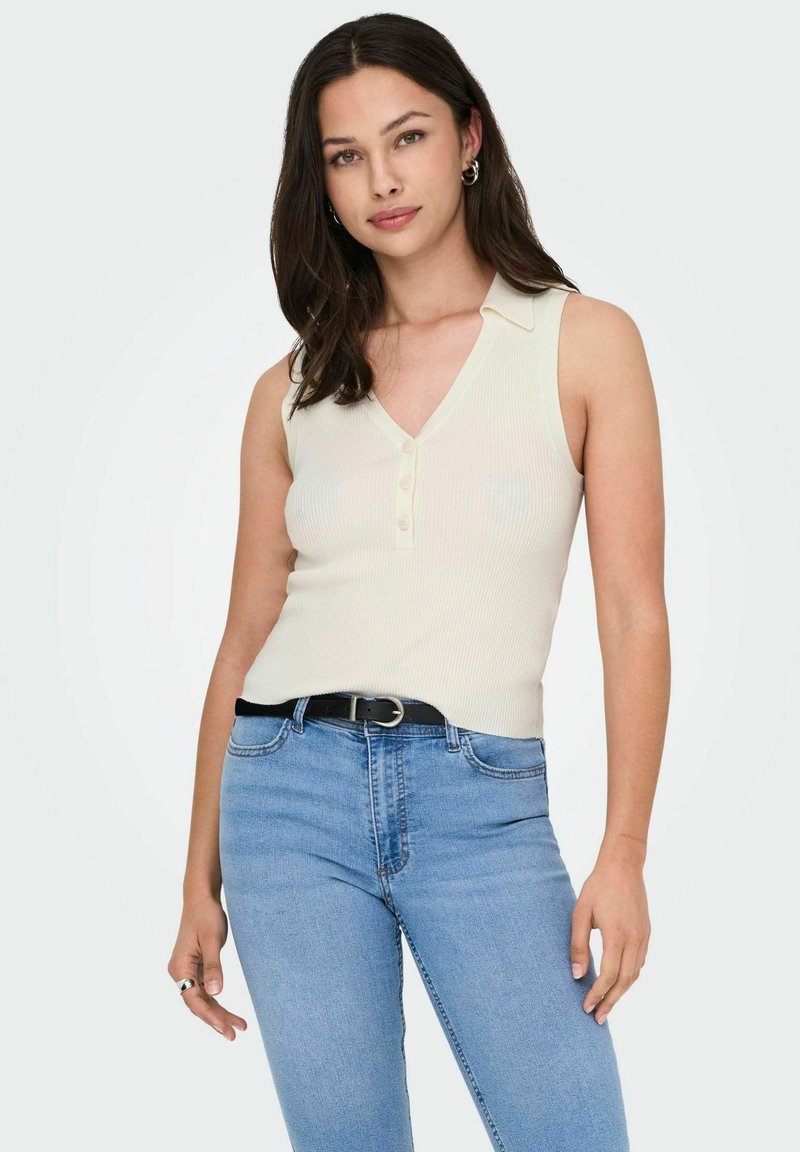 Top senza maniche a costine color crema con scollatura a V e chiusura a bottoni, abbinato a jeans azzurri a vita alta e una cintura nera.
