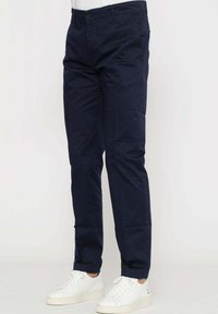 Pantaloni di cotone blu navy con vestibilità dritta, caratterizzati da un bottone di chiusura, tasche laterali e una superficie liscia, abbinati a sneaker bianche.