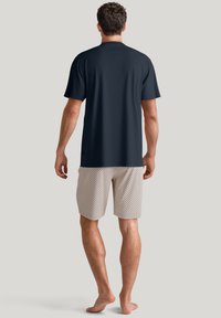 Marineblauwe, kortemouwen shirt gecombineerd met lichte, gemusterde shorts. Het shirt heeft een gladde, ontspannen pasvorm, terwijl de shorts een geometrisch ontwerp hebben.