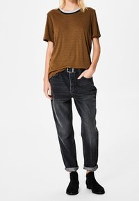 Brun kortærmet t-shirt med en kontrastfarvet blå halsudskæring, parret med sorte denim jeans med opfoldede ærmer og sorte ankelstøvler.