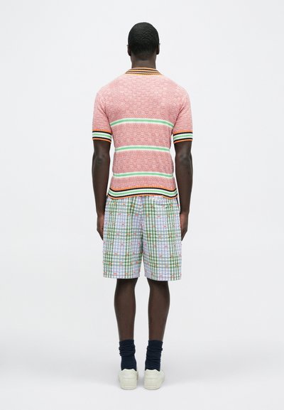 Κοντομάνικο πουκάμισο με κόκκινο και λευκό μοτίβο και πράσινες και μαύρες ρίγες, συνδυασμένο με καρό σορτς σε πράσινο, λευκό και με λουλουδάτες λεπτομέρειες.