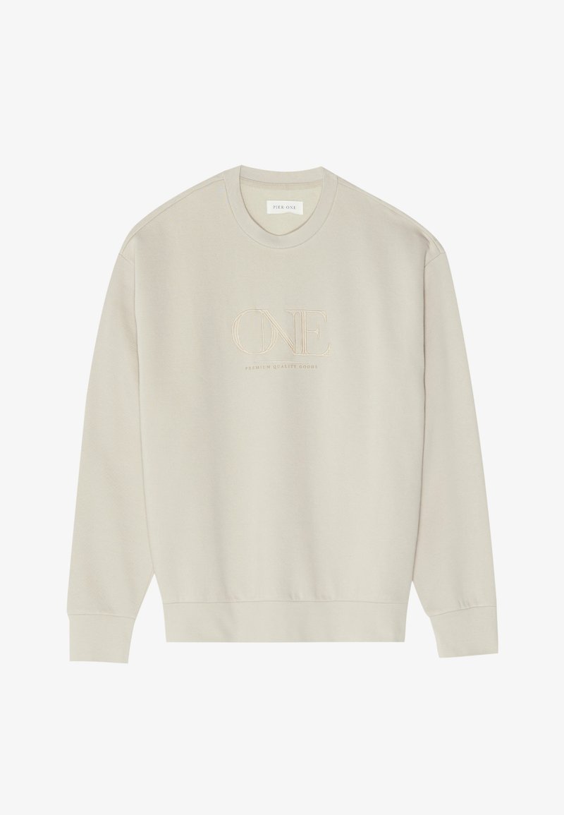 Bēša džemperis ar apaļu kaklu, garām piedurknēm un ribotām aprocēm. Izšuvums ar vārdu "ONE" un tekstu "PREMIUM QUALITY GOODS" uzšūts ar nostrādātas krāsas diegu.