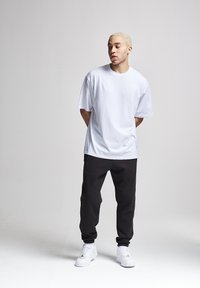 Weißes Baumwoll-T-Shirt, kombiniert mit schwarzen Jogginghosen und weißen Turnschuhen. Das Outfit hat eine bequeme Passform und ein schlichtes Design ohne sichtbare Muster.