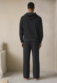 Mørkegrå hoodie og matchende bukser lavet af et blødt, struktureret stof. Hoodien har snoretræk og ribbede manchetter, mens bukserne har en baglomme.