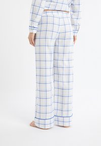 Pantalon à carreaux blancs avec des lignes bleues, présentant une coupe décontractée et une taille élastique. Le tissu semble doux, avec des coutures visibles le long des ourlets.