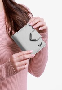 Compact gray wallet made of textured leather, featuring a magnetic closure and a geometric accent. Handheld against a light background.