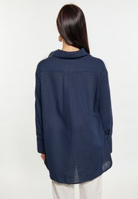 Camicia blu navy con colletto, maniche lunghe e vestibilità rilassata. Presenta uno yoke posteriore e un orlo arrotondato per un tocco di stile. Tessuto leggero.