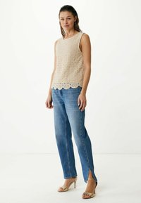 Beige kant top met een gerafeld zoom, gecombineerd met lichtblauwe rechte jeans met zijsplitten en gouden sandaaltjes met hak.