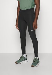 Black athletic leggings with a smooth texture, high waistband, and white logo on the lower leg. Paired with green and white running shoes.