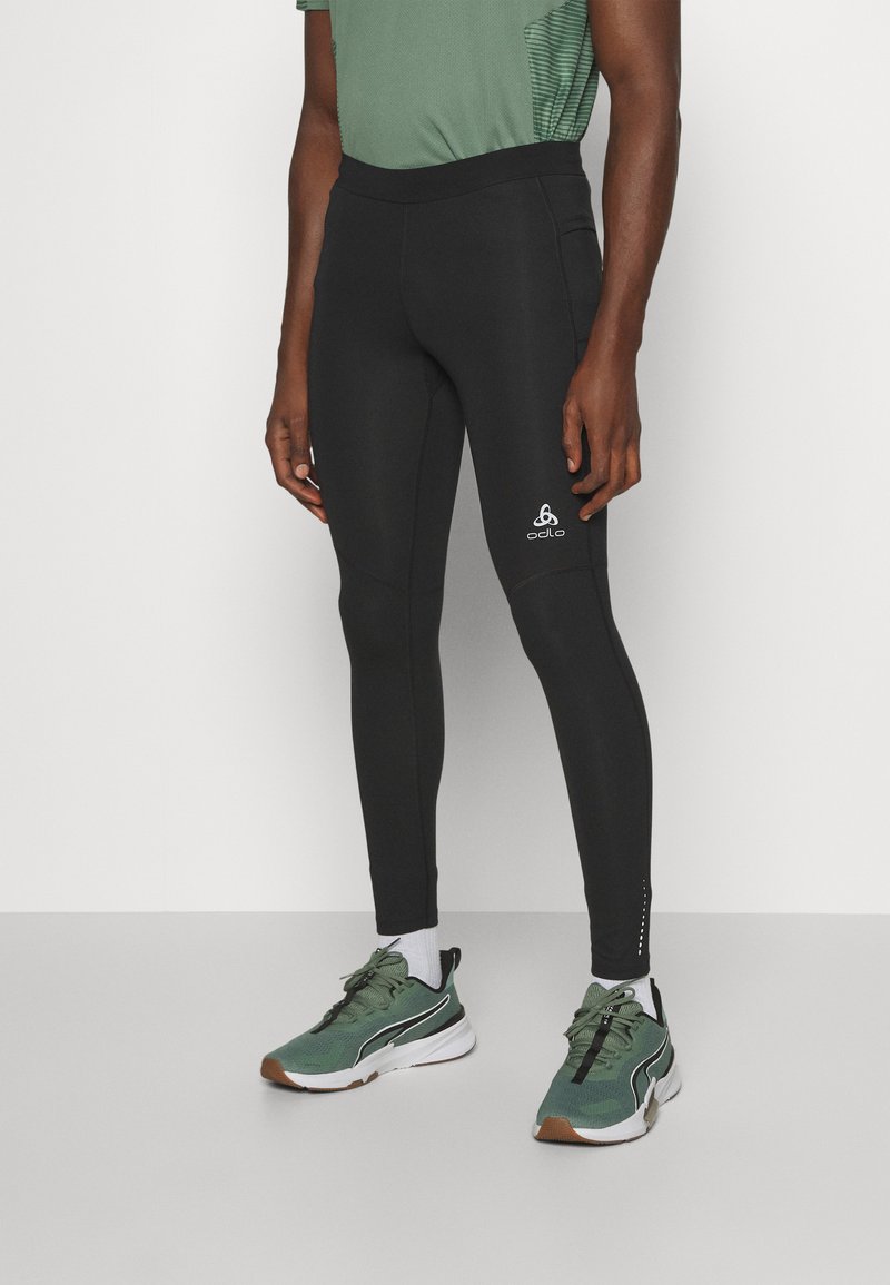 Black athletic leggings with a smooth texture, high waistband, and white logo on the lower leg. Paired with green and white running shoes.