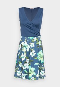 Blå omlottklänning med en enfärgad överdel och kjol med blommönster i vitt och gröna blad mot en marinblå bakgrund.