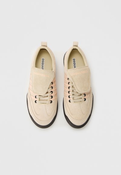 Baskets en daim beige avec un design superposé, présentant des rayures pêche, une semelle en caoutchouc noir et une languette repliée avec un logo embossé.