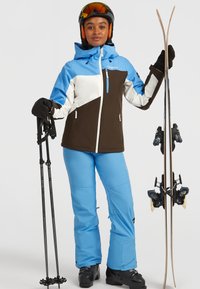 Skikleding met een blauwe, witte en bruine jas, bijpassende blauwe broek, zwarte handschoenen en ski's met bindingen, allemaal op een effen achtergrond.
