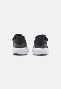 Zapatillas deportivas negras con un upper de tela texturizada, con acentos en rosa y una suela de goma blanca. La vista trasera muestra un diseño de talón acolchado.