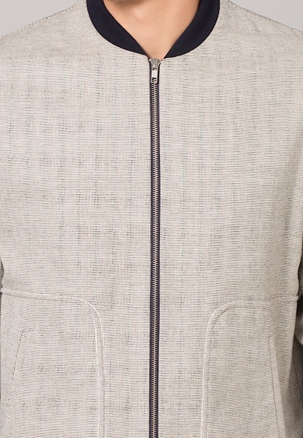 Veste beige texturée à fermeture éclair portée par une personne, avec col noir, poches avant visibles et tirette de la fermeture éclair argentée centrée.