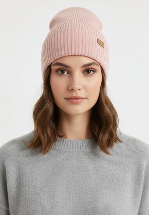 Lichtroze gebreide muts met geribbelde textuur en gestikte details, met een klein bruin leren label; informeel gedragen over bruin haar.