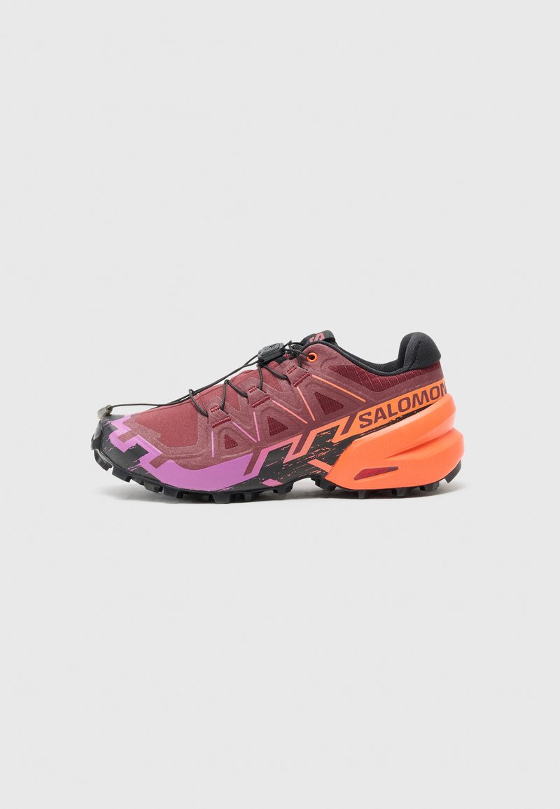 Trail running-sko med en design i vinröd, lila och svart, texturerad ovandel och framträdande orangea accenter på hälen.