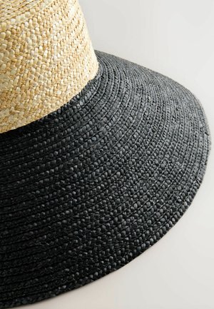 Cappello a tesa larga con design intrecciato, con parte superiore in paglia naturale e parte inferiore intrecciata nera, creando un aspetto bifacciale distintivo.