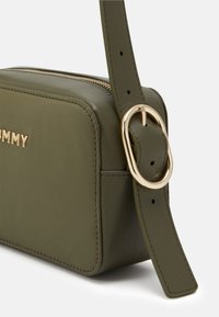 Olivengrøn crossbody taske i glat falsk læder, med en guldtonet spænde på den justerbare rem og en lynlåslukning.