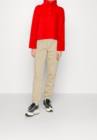 Czerwony krótki polarowy sweter z wysokim kołnierzem, w połączeniu z beżowymi spodniami dresowymi. Czarnobiałe sneakersy z wielokolorowymi sznurówkami dopełniają stylizację.