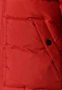 Section d'une doudoune rouge avec une poche visible, dotée d'un bouton noir et d'un tissu texturé matelassé pour l'isolation. Finition de surface lisse.