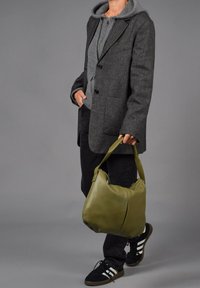 Olijfgroen leren handtas met een ronde vorm en een enkele schouderriem. Draagt een grijze hoodie, zwarte broek en zwarte sneakers.