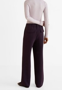 Pantalon large violet foncé avec une texture lisse, taille élastique et deux poches arrière ; modèle vu de dos.