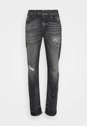 Tmavě šedé úzké džíny s vybledlými a opotřebovanými detaily, včetně drobných trhlin a skvrn od barvy na předních stehnech a kolenou.