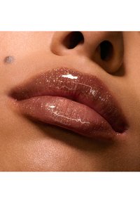Klart læbeglans med en glitrende finish, der fremhæver fyldige, glatte læber med en blød pink-brun nuance og subtile glitrende accenter.