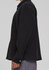 Svart, texturerad långärmad skjorta med rundad fåll, knäppte manschetter och krage. Sidokilar förbättrar flexibilitet och komfort.